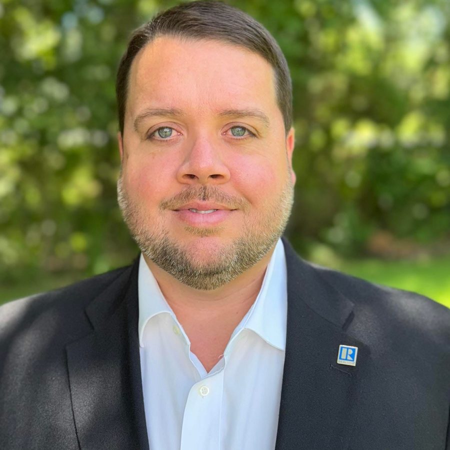 Portrait of Robbie Stockton, Mobile, Alabama real estate agent, smiling in a dark blazer outdoors